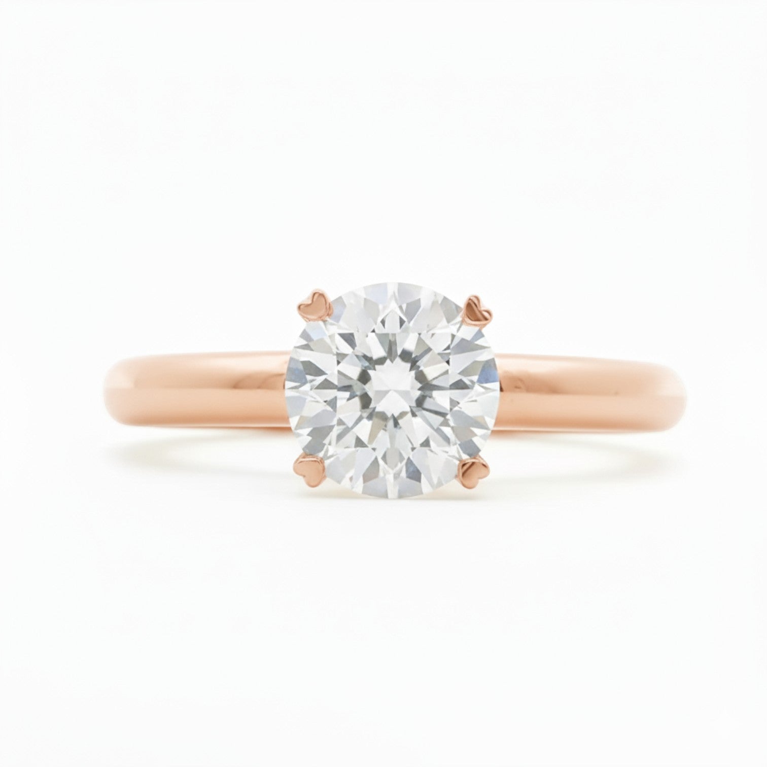 A classic solitaire engagement ring with 4 heart prongs in warm 18K rose gold — Diamond Ateliers.