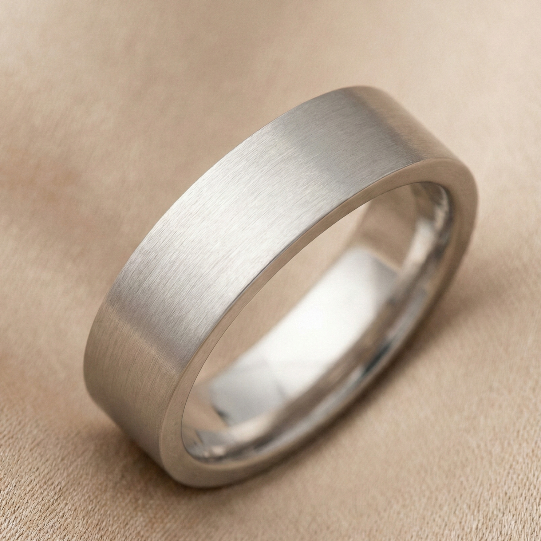 Platinum men’s wedding band featuring a wide matte brushed finish and smooth rounded inner edges, photographed in soft champagne studio lighting on a fabric backdrop