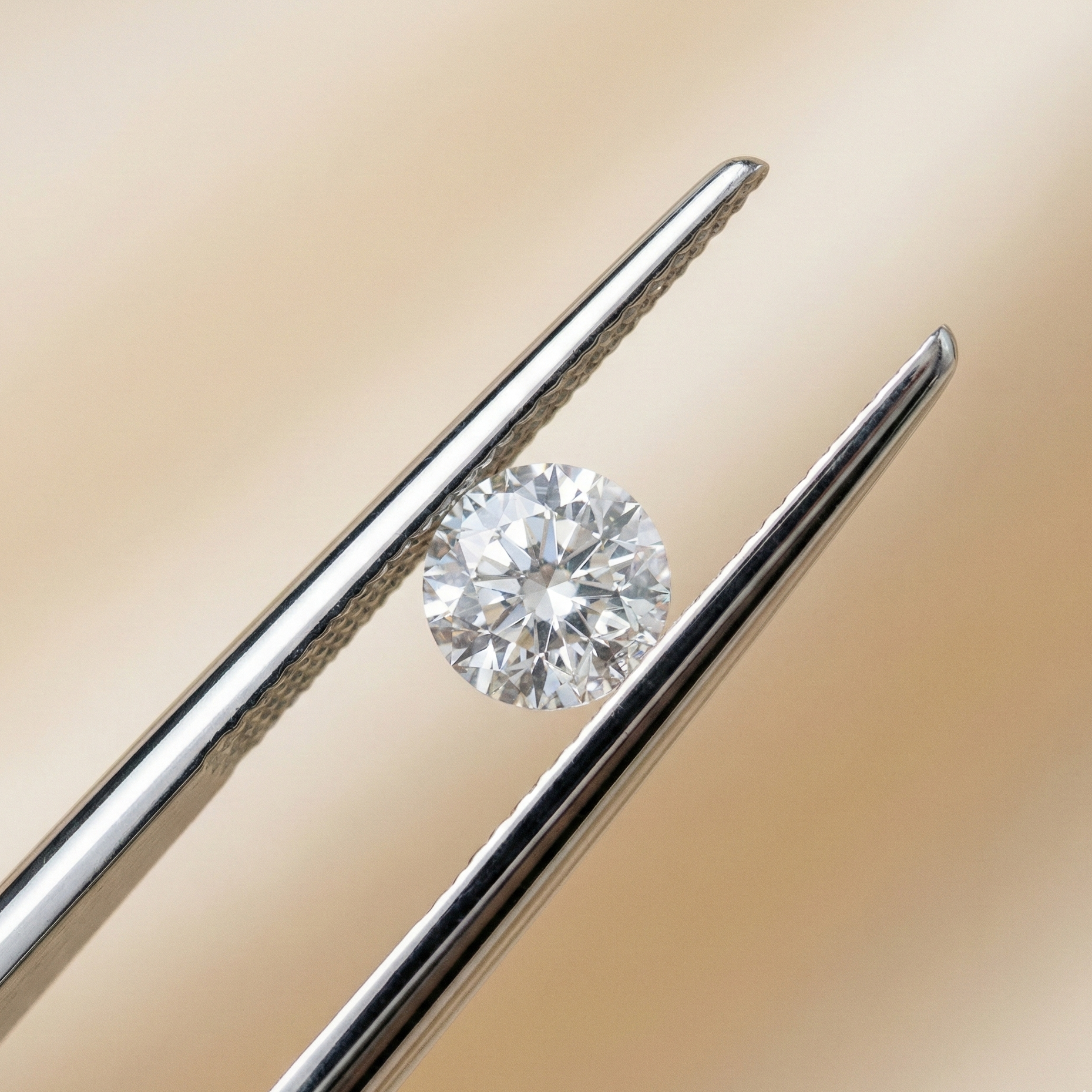 A high-resolution macro photograph featuring a sparkling round brilliant-cut diamond held securely by stainless steel jeweler's tweezers. The diamond catches bright, neutral studio light, emphasizing its clarity and facets, set against a smooth, out-of-focus champagne-beige background.