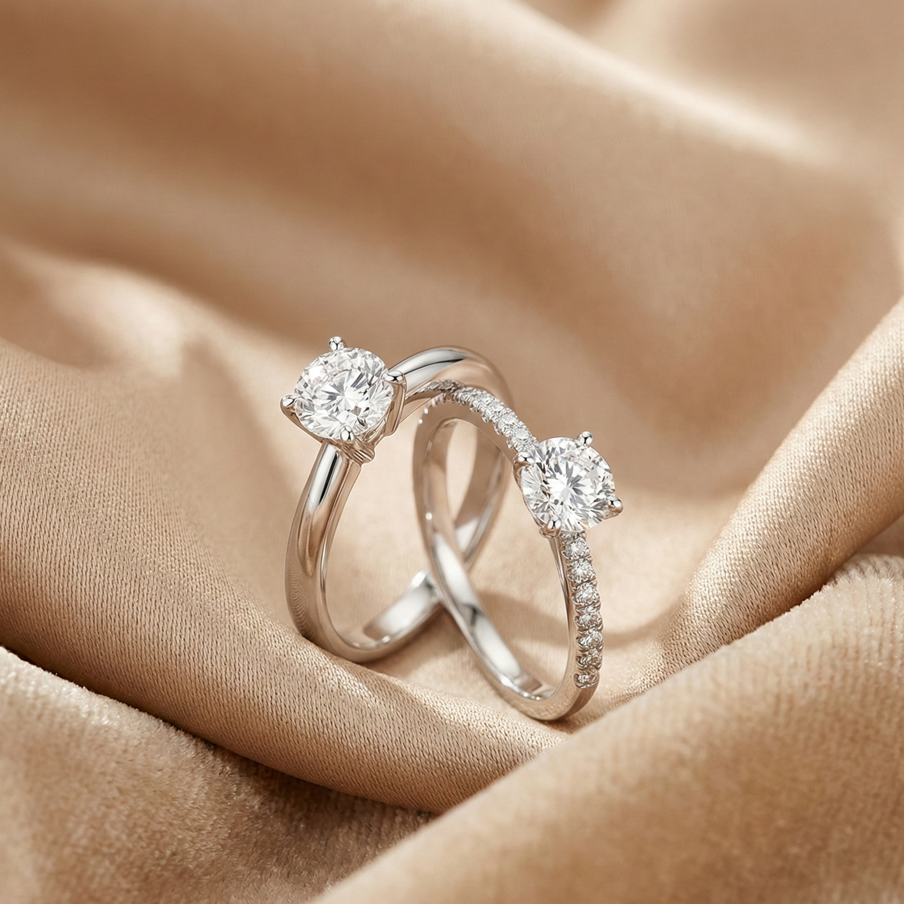 Two white gold engagement rings — one classic solitaire and one pavé band — displayed on champagne fabric