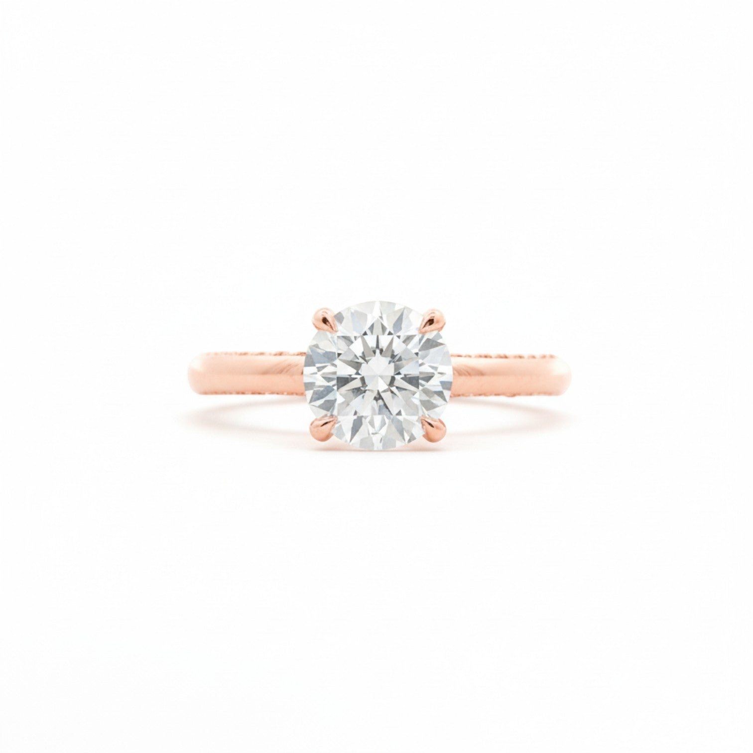 A four-prong round diamond solitaire engagement ring in warm 18K rose gold — Diamond Ateliers.