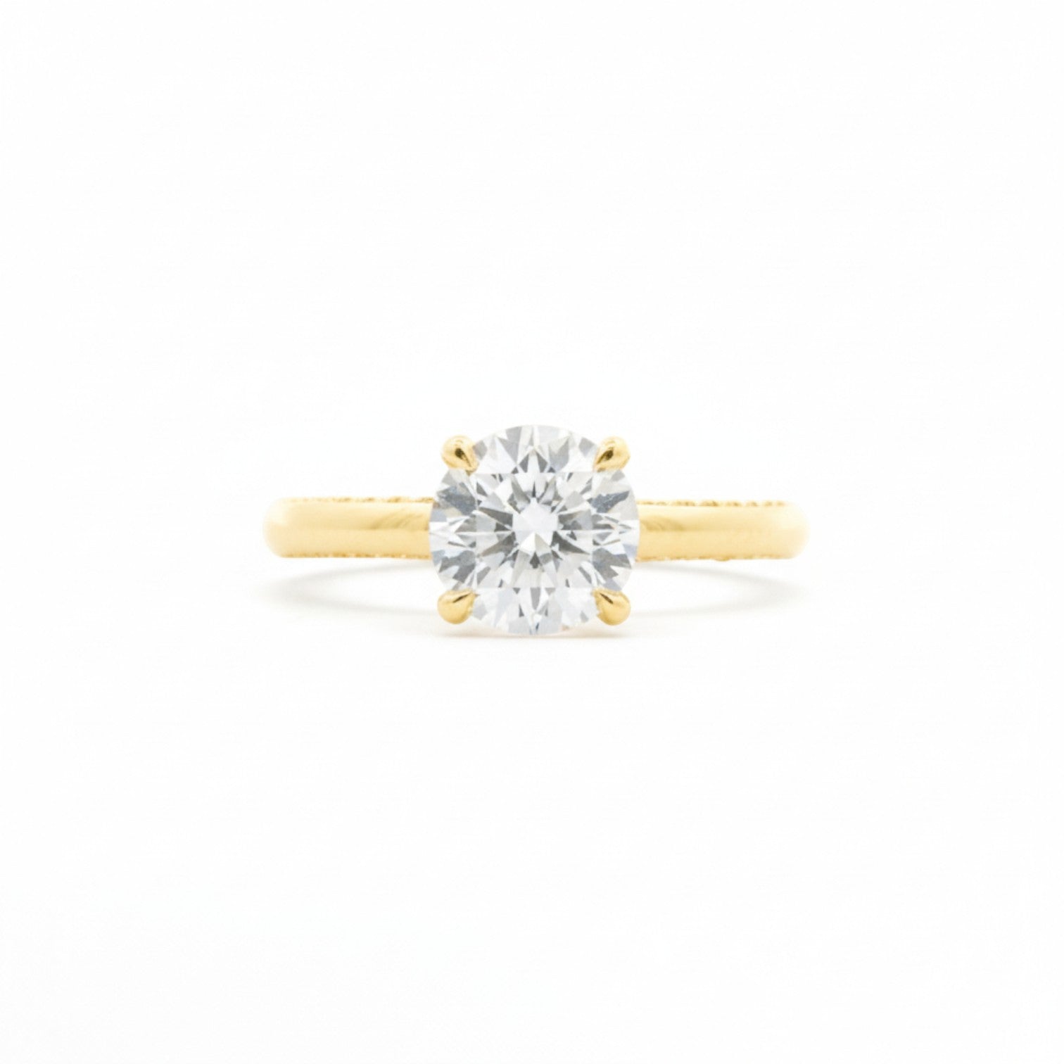 A four-prong round diamond solitaire engagement ring in warm 18K Yellow gold — Diamond Ateliers.
