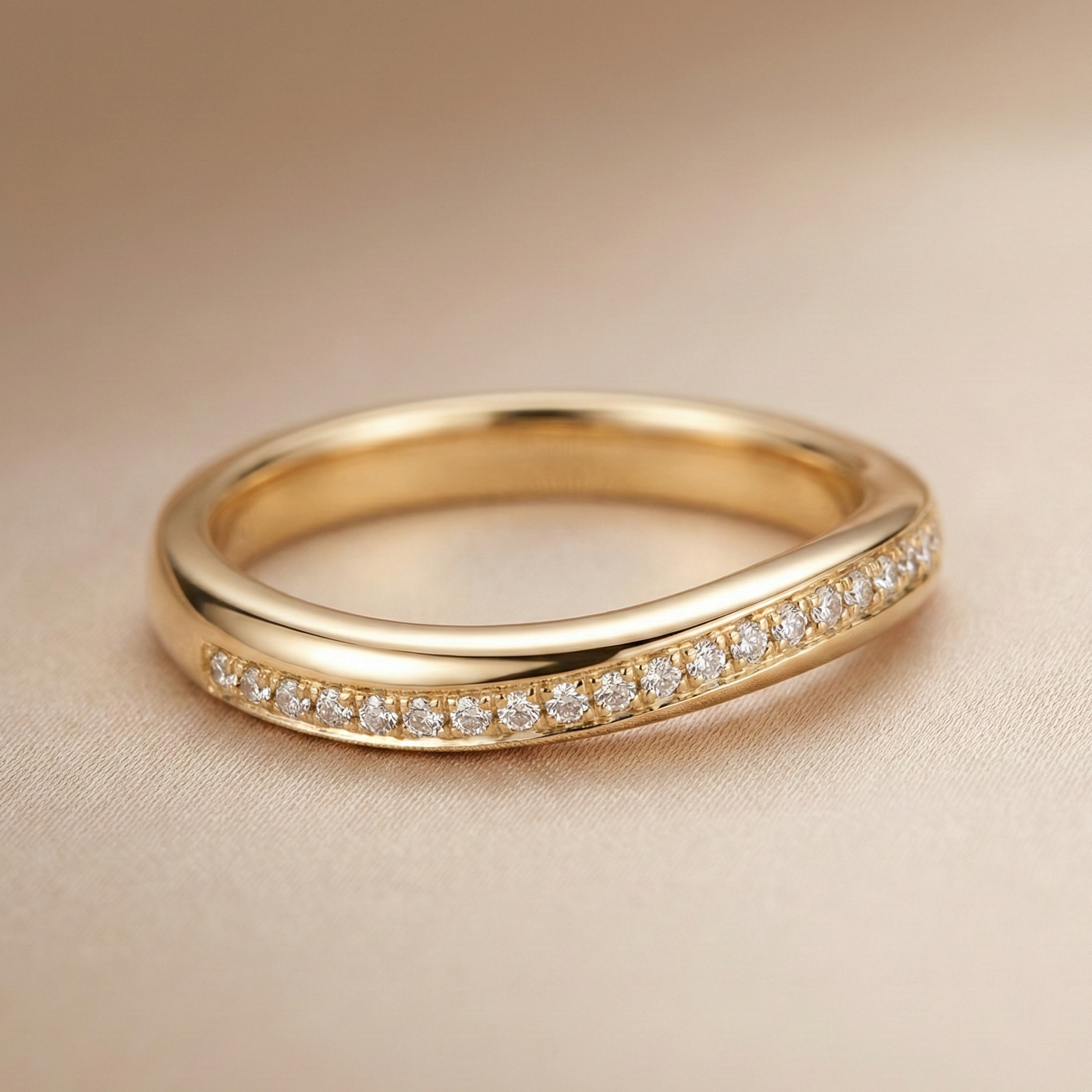 18K yellow gold channel-set diamond wedding band featuring a sleek curved profile and a row of round brilliant diamonds, photographed in soft champagne studio lighting.