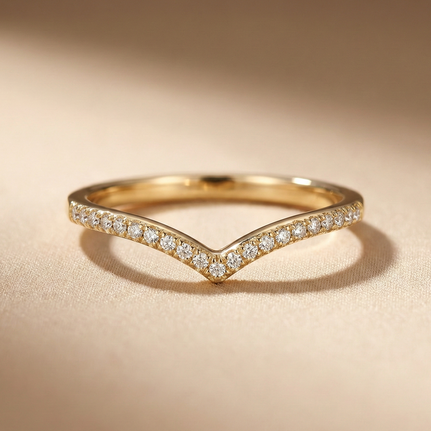 18K yellow gold V-shape pavé diamond band featuring a contoured chevron silhouette and round brilliant diamonds, photographed in warm studio lighting on a champagne fabric backdrop.