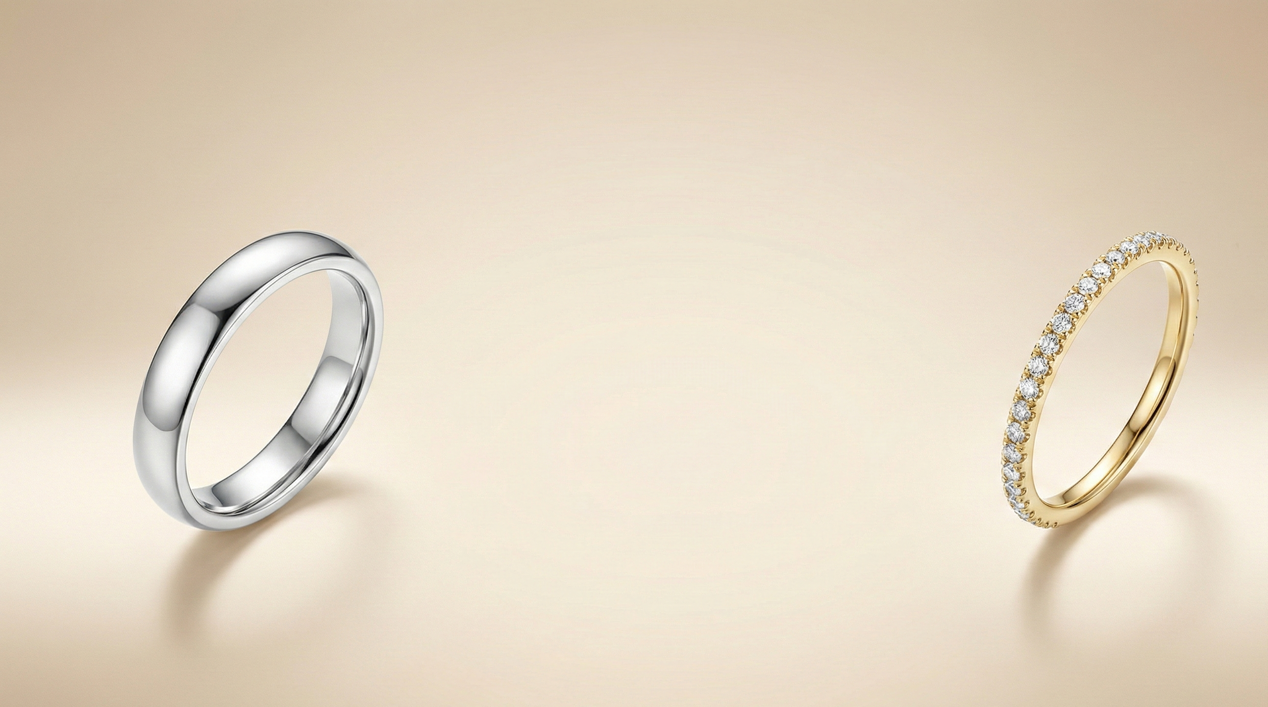 A studio photograph of two contrasting wedding rings placed on a smooth, solid beige background. On the far left is a plain, high-polish white gold or platinum band with a rounded profile. On the far right is a delicate yellow gold band set with a continuous row of sparkling pavé diamonds. The center of the image features open negative space, suitable for text or branding.